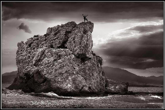 A Guy, arms upraised, atop a big dramatic rock.